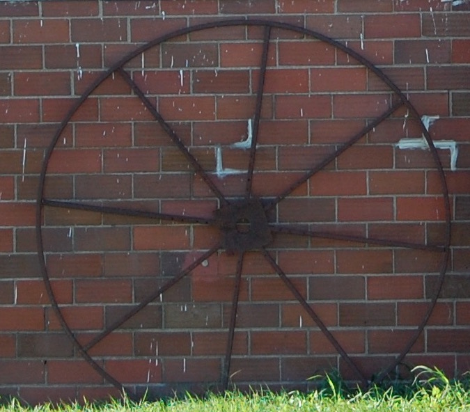 large wheel with spokes in front of brick wall